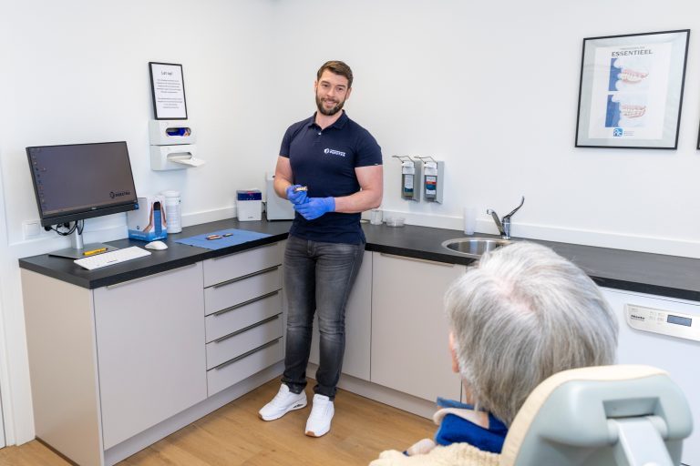 Tandprotheticus legt de behandeling uit aan een patient in de praktijk met witte kasten en apparatuur