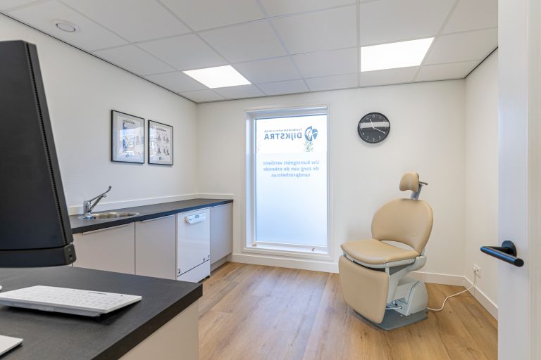 Moderne behandelkamer met beige behandelstoel, witte kasten en professionele apparatuur