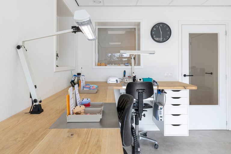 Moderne behandelkamer met behandelstoel, lamp en unit in witte inrichting