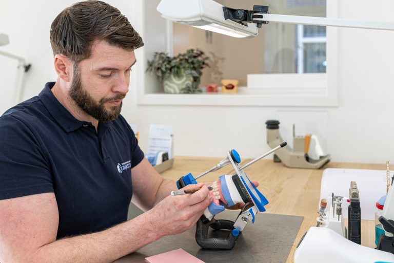 Tandtechnicus werkt aan een kunstgebit in een articulator aan de werkbank