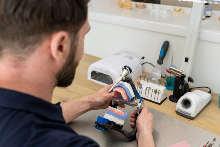 Tandtechnicus controleert een gebitsprothese in een articulator in het laboratorium
